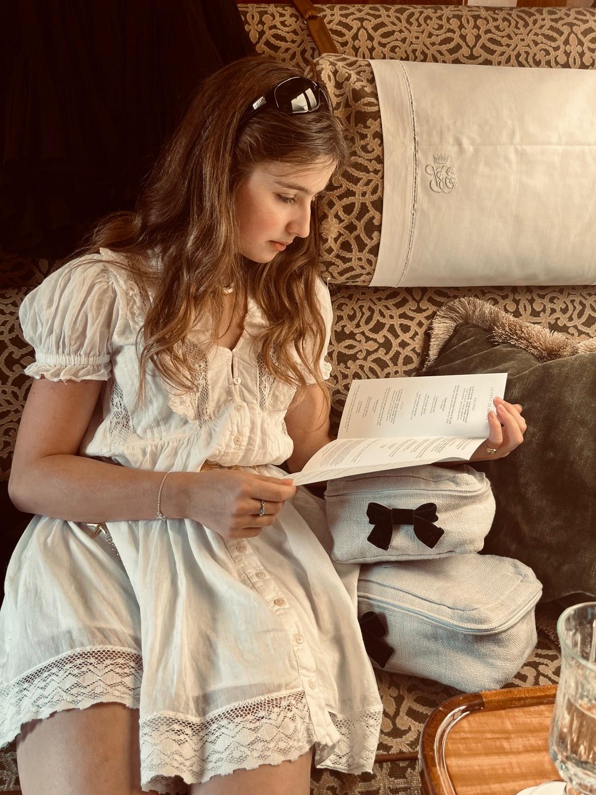 YOUNG WOMAN SITTING ON TRAIN IN flowing white dress with packing cubes on the patterned seat