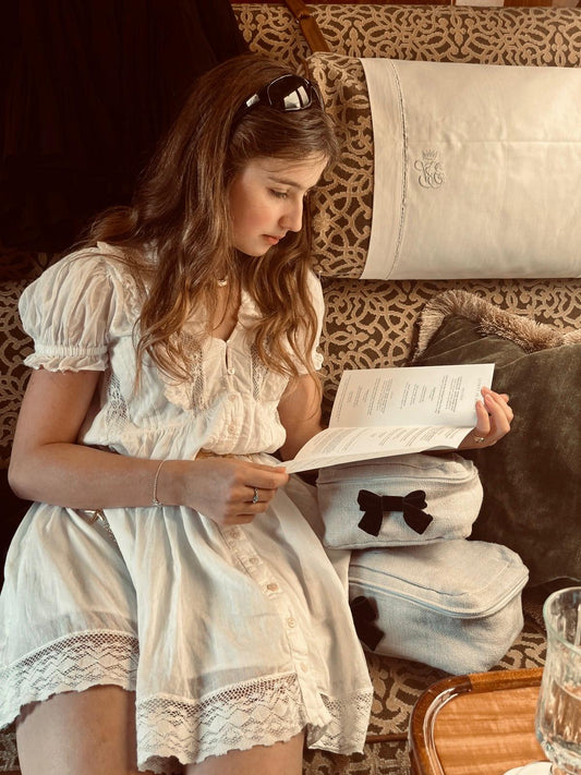 YOUNG WOMAN SITTING ON TRAIN IN flowing white dress with packing cubes on the patterned seat